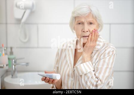 Grauhaarige Frau im Pyjama, die sich im Spiegel anschreckt Und frustriert Stockfoto