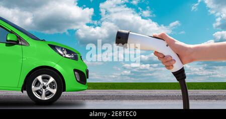 Hand mit Ladegerät auf einem Hintergrund von Elektroauto Stockfoto