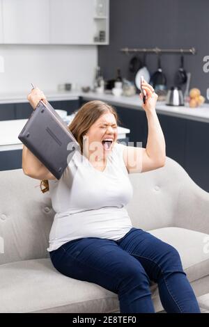 Wut, Wut, Wut mit Laptop in der Hand junge übergewichtige Mädchen zu Hause bleiben während der Quarantäne. Selbstisolierung als Prävention. Arbeiten entfernt Konzept Stockfoto