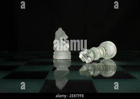 Weiß undurchsichtige Schachfigur Ritter und gefallener König isoliert auf Ein Schachbrett mit Schachbrettmuster und schwarzem Hintergrund Stockfoto