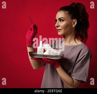 Junge hübsche Frau Arzt Gynäkologe in Latex-Handschuhe steht und Pinzette in der Hand halten und medizinisches Werkzeug auf Tablett Stockfoto