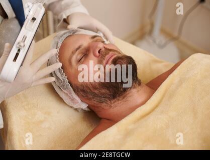 Portrait von bärtigen Mann auf dem Massageliegen Tisch im Schönheitssalon bereit für den Erhalt Mesotherapie. Stockfoto
