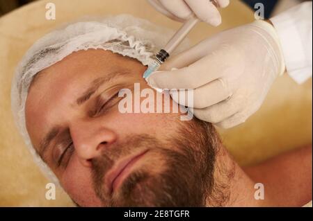 Hände in medizinischen Handschuhen Herstellung Beauty-Injektion für einen schönen Mann in Schönheitssalon. Verjüngungskonzept Stockfoto
