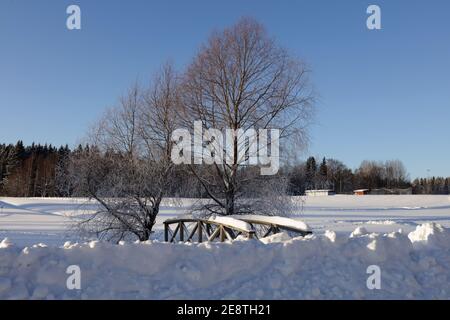 Holzbrücke bei strahlendem Sonnenschein, Winter und Schnee. Bach, Bach umgeben von tiefem Schnee. Stockfoto