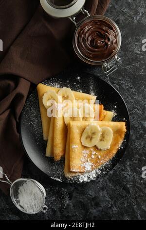 Konzept der leckeren Frühstück mit Crepes mit Zuckerpulver und Banane auf schwarzem rauchigen Hintergrund Stockfoto