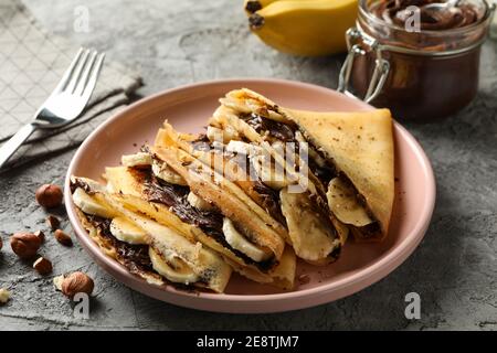 Konzept des leckeren Frühstücks mit Crepes mit Schokoladenpaste, Banane und Nüsse auf grauem Hintergrund Stockfoto