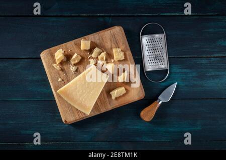 Zerbröckelter Parmesankäse mit einem Messer und einer Reibe, von oben auf dunklem Holzgrund geschossen Stockfoto