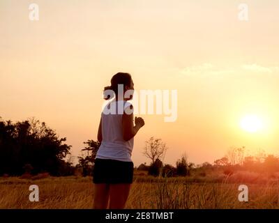Junge Frau läuft auf ländlichen Betonstraße auf schönen hellen Sonnenuntergang Himmel Hintergrund in der Nähe des Sommerfeldes. Lifestyle Abend Lauf Hintergrund. Fitness und Stockfoto