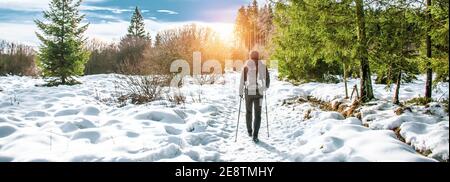 Wandermännchen mit Rucksack und Nordic Walking Stöcken im Schnee. Stockfoto