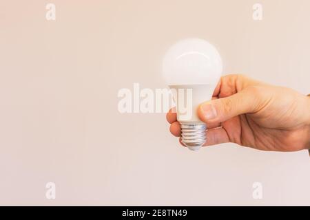 Mann Hand hält beleuchtete Glühbirne vor beigem Hintergrund Stockfoto