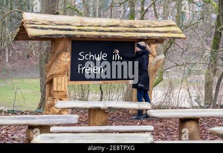 Die Lehrerin schreibt auf einer Tafel den deutschen Ausdruck "Schule im Freien". Ein Klassenzimmer im Wald ist für den Unterricht du qualifiziert Stockfoto