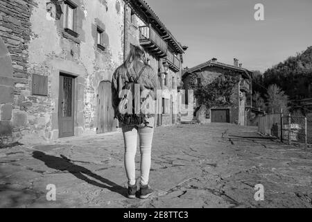 Junge Frau suchen Smartphone zu Fuß mit Mode Jeans Jacke und Rucksack.Tourist Reisekonzept in alten mittelalterlichen Dorf Rupit, Barcelona, Stockfoto