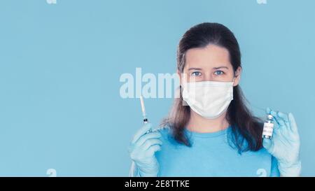 Ärztin mittleren Alters in medizinischer Maske und Handschuhen mit Covid-19 Coronavirus-Impfstoff und Spritze. Konzept der erfolgreichen Impfentwicklung und Beginn der Immunisierung Stockfoto