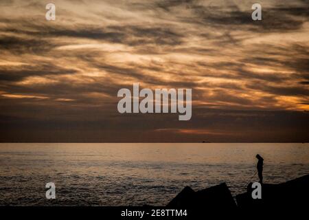 Barcelona, Spanien. Februar 2021. Ein Fischer steht auf einem Pier und hält eine Angelrute, kurz bevor die Sonne über dem Mittelmeer in Barcelona aufgeht. Quelle: Jordi Boixareu/Alamy Live News Stockfoto