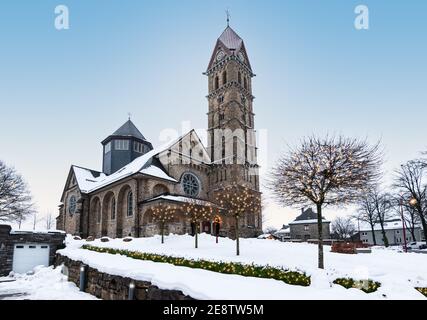 Schöne Kirche in Butgenbach umgeben von einer Winterlandschaft mit beleuchteten Weihnachtslichtern in den Bäumen. Stockfoto