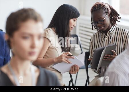 Portrait von zwei jungen Frauen im Gespräch, während sie im Publikum bei einer Geschäftskonferenz oder einem Seminar sitzen, Kopierraum Stockfoto