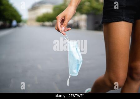 Zugeschnittenes Bild von Frau Hand werfen eine Maske in die Straße Stockfoto