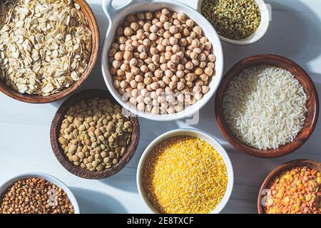 Verschiedene trockene Cerealien und Hülsenfrüchte in weißen und hölzernen Schalen, weißer Hintergrund. Veganes Protein-Konzept. Stockfoto