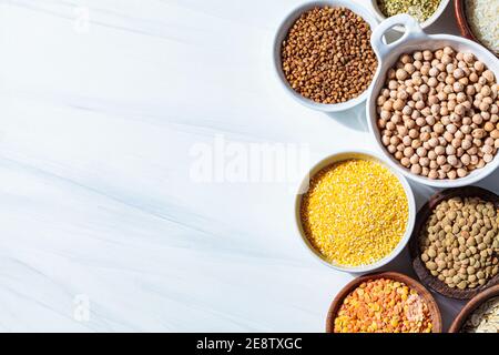 Verschiedene trockene Cerealien und Hülsenfrüchte in weißen und hölzernen Schalen, weißer Hintergrund. Veganes Protein-Konzept. Stockfoto