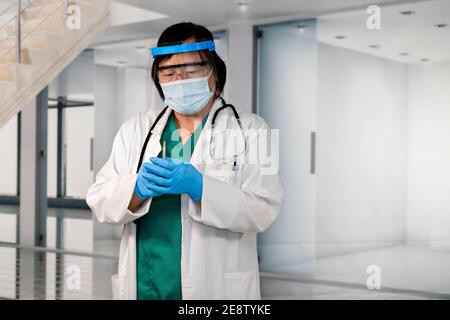 Asiatische Ärztin mit Gesichtsschutz und Handschuhe halten eine Spritze mit beiden Händen. Selektiver Fokus. Impfungs- und Gesundheitskonzept. Stockfoto