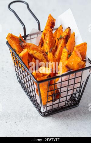 Gebratene Süßkartoffelkeile in einem Metallkorb, grauer Hintergrund. Veganes Lebensmittelkonzept. Stockfoto