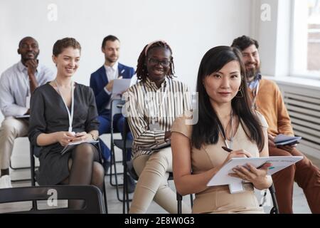 Multiethnische Gruppe von Geschäftsleuten, die auf die Kamera schauen und lächeln, während sie bei einer Geschäftskonferenz oder einem Seminar im Publikum sitzen, Platz kopieren Stockfoto