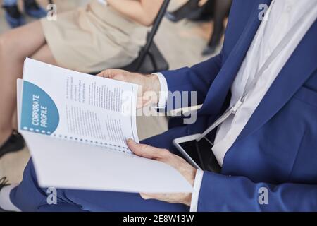 Beschnittene Seitenansicht des nicht erkennbaren Mannes, der den Projektflyer-Planer hält, während er bei einer Geschäftskonferenz im Publikum sitzt, Platz kopieren Stockfoto