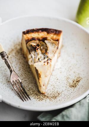 Stück vegan milchfrei zuckerfrei frisch hausgemachter Birnenkäse in rustikalem Teller und Gabel über weißem Marmortisch-Hintergrund, selektiver Fokus, Nahaufnahme. Modernes vegetarisches gesundes Dessertkonzept Stockfoto