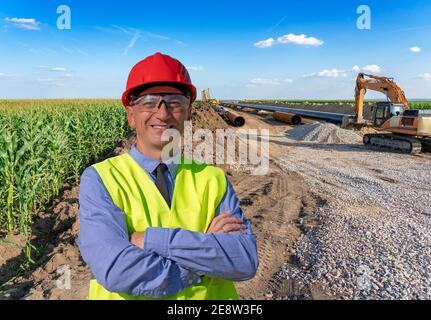 Glücklicher Manager in Red Hardhat, Blue Shirt und Yellow Vest Blick auf Kamera. Portrait von Baumeister, Supervisor, Öl- und Gasingenieur oder Mana Stockfoto