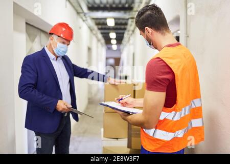 Unternehmer mit Gesichtsmaske und Lagermitarbeiter Überprüfung einer Lieferung Von Waren Stockfoto