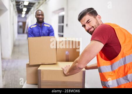 Zwei Arbeiter transportieren Pakete zum Lager des Spediteurs Der Schubkarren Stockfoto