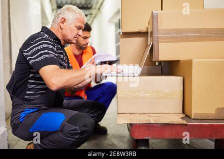 Zwei Lagerarbeiter am Laptop planen den Paketversand Im Online-Handel Stockfoto