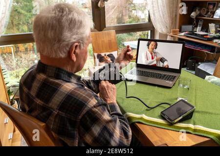 Symbolisches Bild der Telemedizin, ältere Patienten sprechen mit einem Arzt in einer Videokonferenz, von zu Hause aus wird die Verwendung eines Blutdruckmessmonitors erklärt, Stockfoto