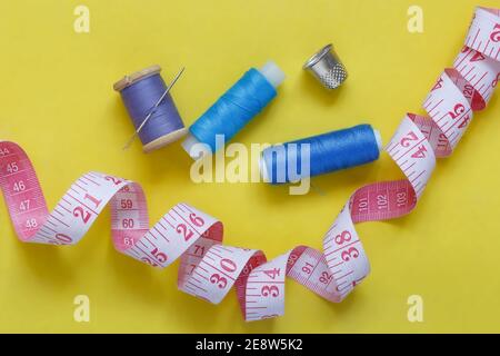 Spulen aus Faden, eine Nadel, ein Dimmel und ein Maßband auf gelbem Hintergrund. Blick von oben. Stockfoto