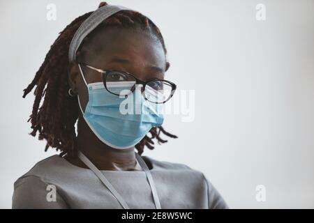 Kopf- und Schulterporträt einer jungen afroamerikanischen Frau, die Maske und Brille trägt, während sie vor weißem Hintergrund steht und auf die Kamera schaut, Co Stockfoto