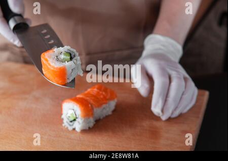 Cook schneidet Sushi und hält ein Stück auf der Klinge Eines Messers Stockfoto