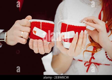 Tassen in gestrickten roten Bezügen mit Herzen mit heißem Tee Und Dampf in den Händen der Liebhaber Stockfoto