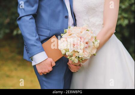 Zarte schöne Hochzeit Bouquet von rosa Pfingstrosen Rosen und Orchideen in den Händen der Braut, in den Händen des Bräutigams braun Buch Stockfoto