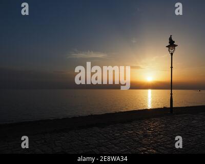 Silhouette der Möwe sitzt auf Lampe während romantischen Sonnenuntergang über dem Meer. Horizontale Aufnahme. Stockfoto