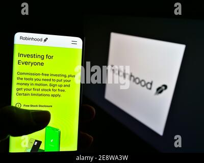 Person, die Telefon mit der Website des US-Finanzdienstleisters Robinhood Markets Inc. Auf dem Display vor dem Logo hält. Fokus auf Telefonbildschirm. Stockfoto