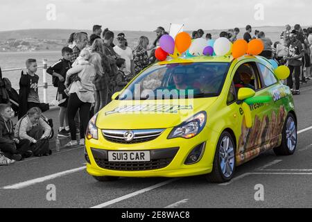Subway gelb Vauxhall Corsa Auto mit Ballons nimmt an der Prozession Parade in Weymouth Carnival, Weymouth, Dorset UK im August - Farbe popped Stockfoto