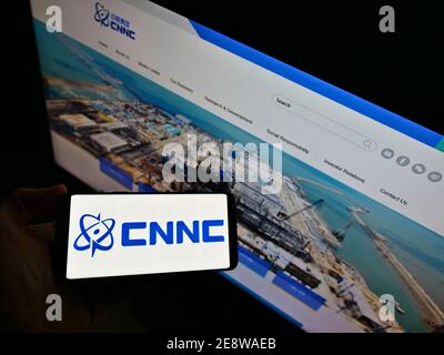 High-Angle-Ansicht der Person hält Smartphone mit Logo der China National Nuclear Corporation (CNNC) auf dem Display mit Website. Fokus auf Telefonbildschirm. Stockfoto