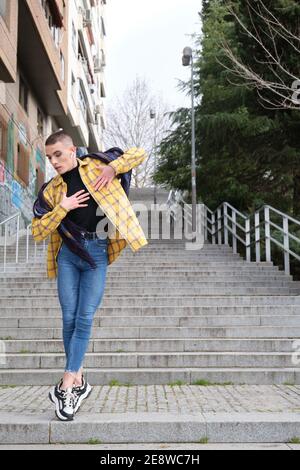 Hübscher junger Mann, der Make-up und Kopfhörer trägt und auf Treppen tanzt. Nicht binäre androgyne Kerl. Stockfoto
