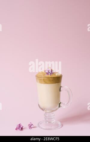 Schöner Dalgon-Kaffee-Drink. Kaffeebecher aus klarem Glas mit Schaumstoff und Fliederblüte auf einem lila rosa Hintergrund. Stockfoto