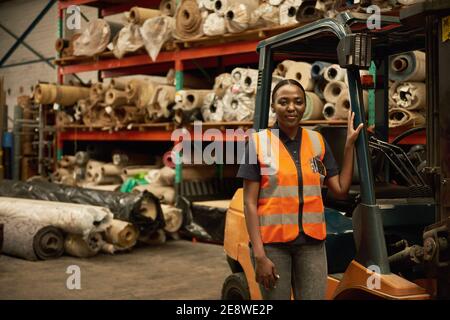 Junge afrikanische Gabelstaplerfahrerin, die in einem Lager steht Stockfoto