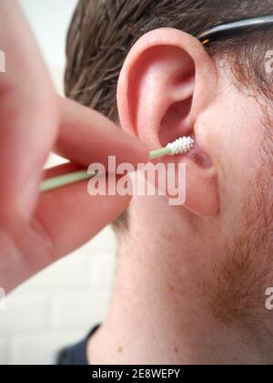 Der Mann reinigt sein Ohr mit einem wiederverwendbaren Q-Tip aus Silikon. Zero Waste Lifestyle-Konzept. Stockfoto