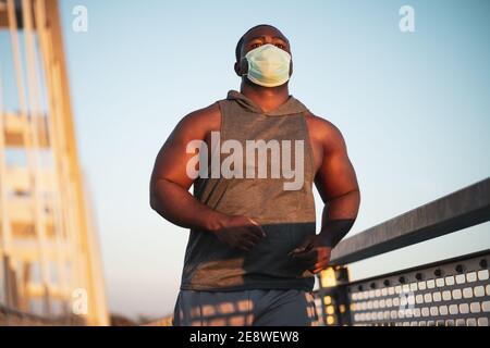 Der junge afroamerikanische Mann joggt mit einer Schutzmaske im Gesicht. Stockfoto