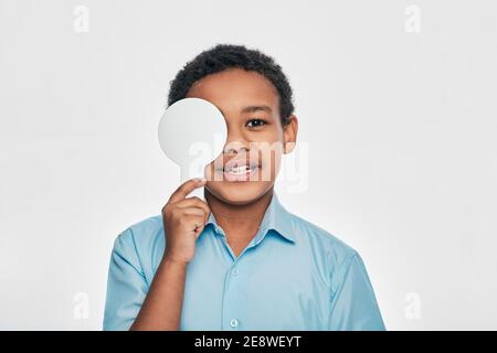 Afroamerikanische männliche Kind mit Augenuntersuchung mit einem Auge bedeckt mit einem ophthalmischen Werkzeug, auf weißem Hintergrund Stockfoto