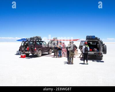 Touristen essen unter einem Sonnenschirm neben ihren Jeeps in der Salzwüste Uyuni, Bolivien Stockfoto