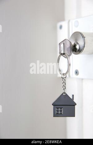 Silberner Hausschlüssel in weißer Tür, mit kleinem Schlüsselanhänger Haus, Tür zum neuen Haus, Haus, Investition, Immobilienkonzept, Raum für Text öffnen